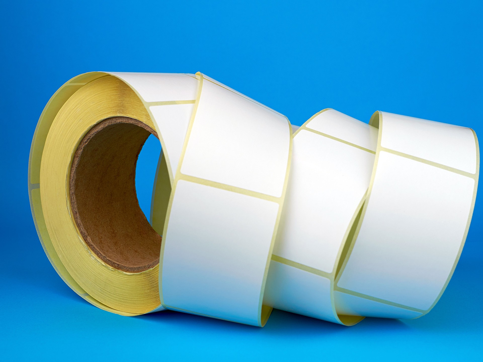 White roll of labels for thermal perforation on a blue background. Babina of self-adhesive stickers. Self-adhesive white label roller for printing or manufacturing.